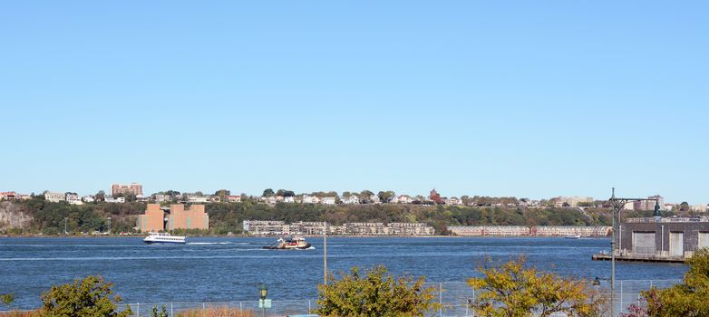 Ferry and work boat navigate the Hudson River in New York City. Weehawken and Hamilton Park in New Jersey are on the opposite riverbank.