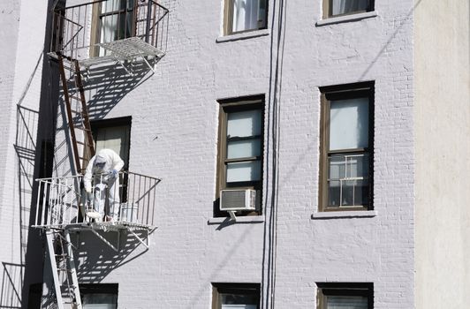 Painter dressed in coveralls, painting metal fire escape white on an apartment building in New York City