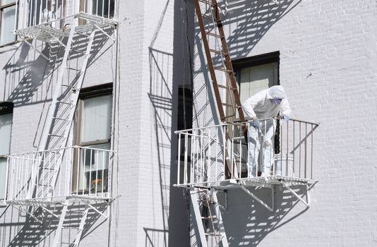 Building painter, dressed in protective overalls, painting metal fire escapes white at the rear of a building in Manhattan, New York City