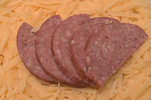 Five red pieces of salami sausages placed over yellow grated cheese as a background