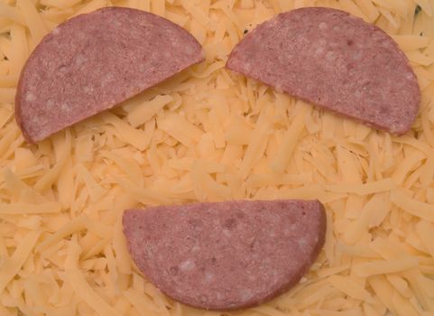three red pieces of salami sausages placed over yellow cheese in shape of smile