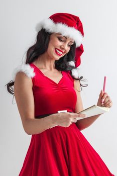 Pretty smiling pin-up Santa girl in red dress with wish list and pencil