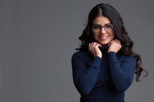 Beautiful blue eyed brunette woman with long curly hair wearing glasses looking directly at the camera and smiling