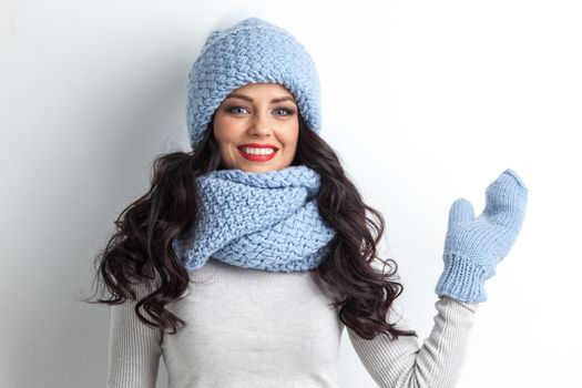 Beautiful woman in warm hat, mittens and scarf waving hand