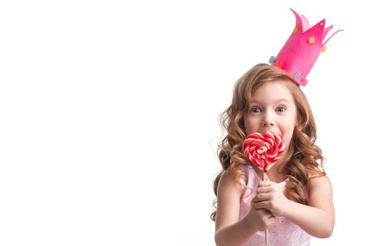 Beautiful little candy princess girl in crown holding big pink heart lollipop and smiling