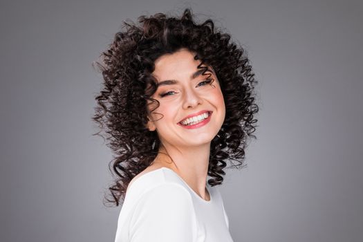 Portrait of amazing beautiful smiling woman with curly hair on gray background with copy space