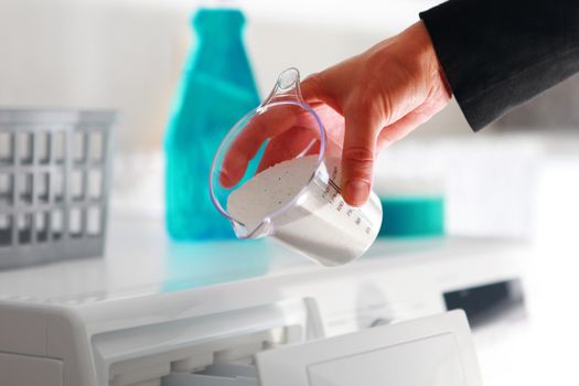 hand of woman that fills detergent from dosing cup in the washing machine