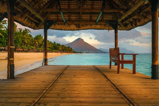 Wonderful view across the pier, on the left the tropical beach and in the background a beautiful mountain illuminated by red during sunset, Mauritius