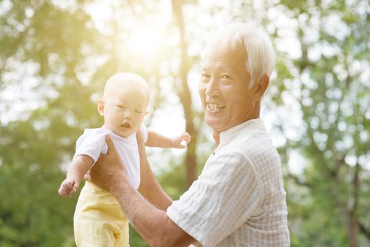 Grandfather holding baby grandson at outdoor park, Asian family, life insurance concept.