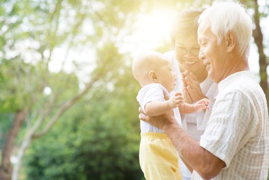 Grandparents holding baby grandson at outdoor park, Asian family, life insurance concept.