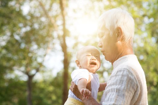 Grandfather and crying baby grandson at outdoor park, Asian family, life insurance concept.