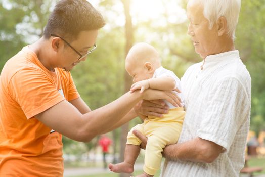 Grandfather and father taking care of baby grandson at outdoor park. Asian multi generations family.