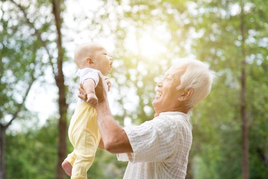 Grandfather holding baby grandchild at outdoor park, Asian family, life insurance concept.