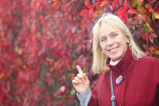 Happy smiling senior woman in autumn park over red leaves background
