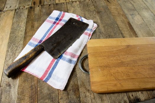 Old chopper and meat board on a wooden kitchen table, black background