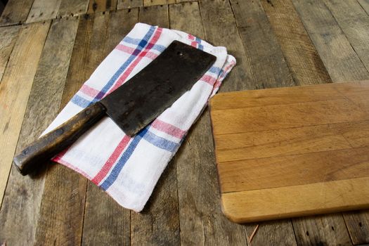 Old chopper and meat board on a wooden kitchen table, black background