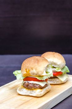 Delicious homemade gourmet cheese burgers made from beef with fresh ingredients placed on wooden platters