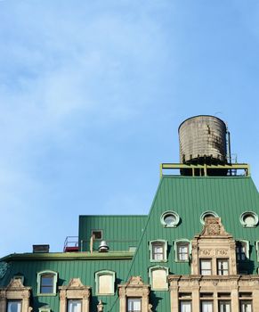 Water tower on the rooftop of a New York City building with a distinctive green roof, against a blue sky