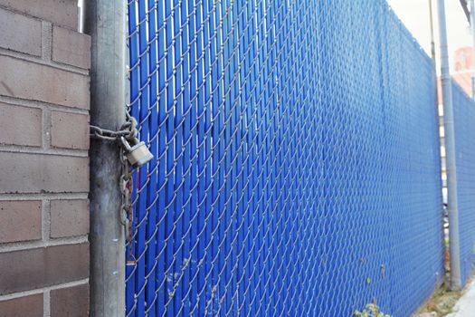 Blue plastic and metal security fence and gate secured with a heavy padlock