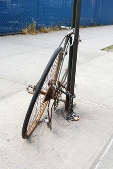 Abandoned broken and rusty bicycle chained to a metal pole on a pavement