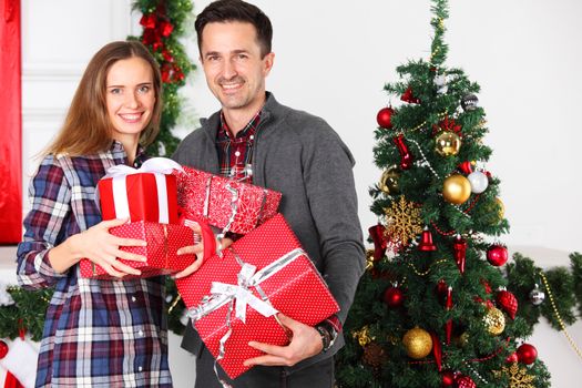 Couple in love sitting next to a nicely decorated Christmas tree, hloding Christmas gifts and smiling