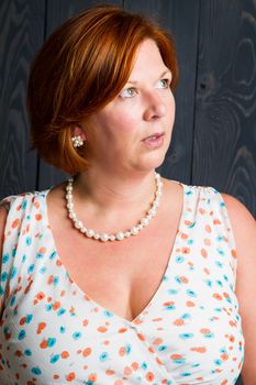 forty something brunette woman wearing a sun dress in front of blue wood panel looking to the right