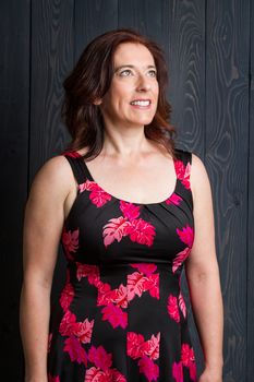 forty something brunette woman wearing a sun dress in front of blue wood panel looking into her right