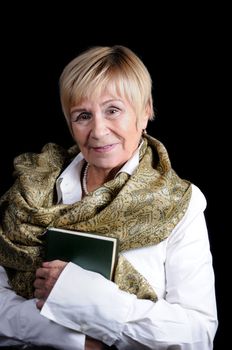 Portrait of an elderly woman with a book in her hands in a white shirt with a shawl on her shoulders against a dark background close-up