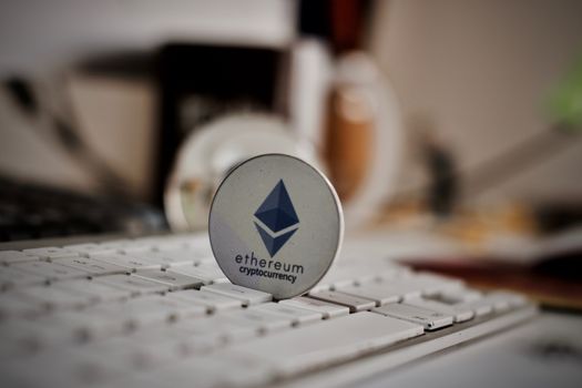 Crypto currency physical grey ethereum token on white keyboard in office.