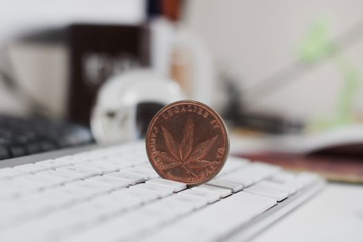 Legalize it. Brass marijuana coin with cannabis leaf on the white keyboard in office.