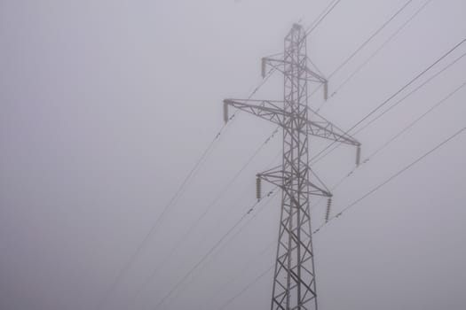electric pylon and power line in morning fog. Dim world in obscure.