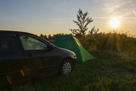 ourist tent and car in green meadow at campsite. Camping place in the meadow in nature park in summer in sunny morning . Adventure travel active lifestyle freedom outdoors. Family time holidays.