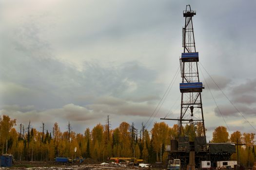The oil drilling rig in a beautiful mixed autumn forest on a cloudy day
