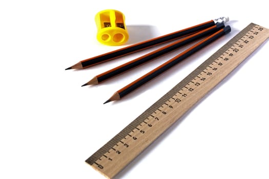 Stationery - Wooden school ruler, sharpener and three graphite pencils on a white background.