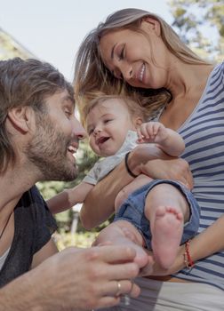 A young beautiful couple are teesing their happy woughing cute baby.