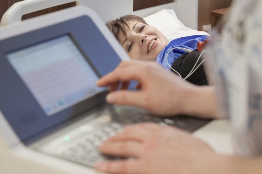 A young happy female patient is getting good news from a doctor, while her heart rate is measured with a monitor in hospital.