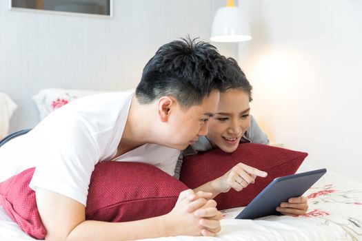 Young Asian Couples lying down and using tablet together in living room of contemporary house for modern lifestyle concept