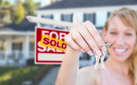 Excited Woman Holding House Keys and Sold For Sale Real Estate Sign in Front of Nice New Home.