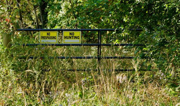 Steel gate with warning signs in the foliage