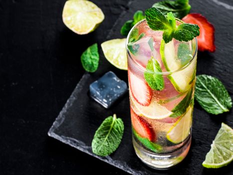 fresh lemonade with strawberry, lime and mint on dark stone background. Cold summer strawberry drink with mint and ice. Strawberry mojito in glass and ingredients. Copy space