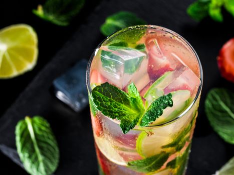 fresh lemonade with strawberry, lime and mint on dark stone background. Cold summer strawberry drink with mint and ice. Strawberry mojito in glass and ingredients
