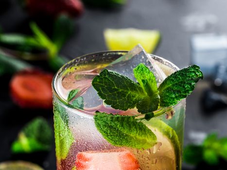 fresh lemonade with strawberry, lime and mint on dark stone background. Cold summer strawberry drink with mint and ice. Strawberry mojito in glass and ingredients