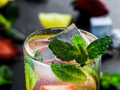 fresh lemonade with strawberry, lime and mint on dark stone background. Cold summer strawberry drink with mint and ice. Strawberry mojito in glass and ingredients