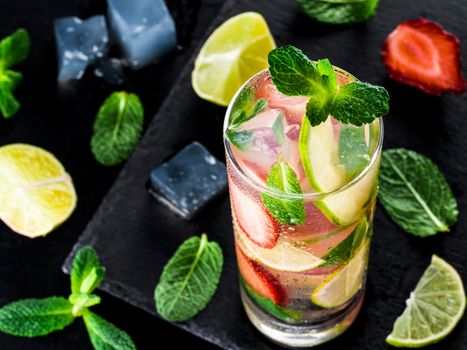 fresh lemonade with strawberry, lime and mint on dark stone background. Cold summer strawberry drink with mint and ice. Strawberry mojito in glass and ingredients