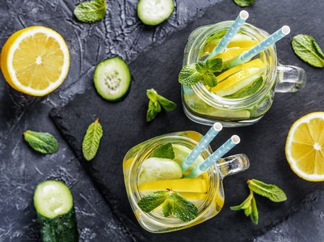 Above view of two mason jar with detox water on dark concrete background. Summer drink with cucumber, lemon and mint. Copy space. Top view or flat lay