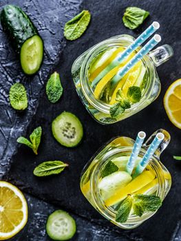 Above view of two mason jar with detox water on dark concrete background. Summer drink with cucumber, lemon and mint. Copy space. Top view or flat lay. Vertical