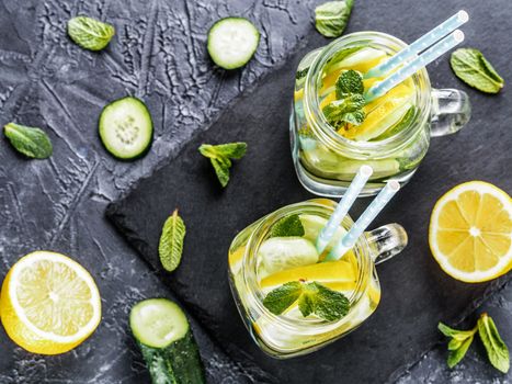 Above view of two mason jar with detox water on dark concrete background. Summer drink with cucumber, lemon and mint. Copy space. Top view or flat lay