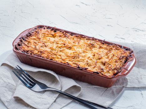 Close up view of appetizing potato casserole with fish, eggs and cream. Potato casserole in serving baking dish on white concrete background