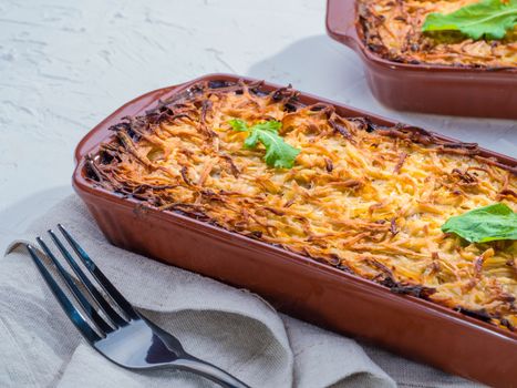 Close up view of appetizing potato casserole with fish, eggs and cream. Potato casserole in serving baking dish on white concrete background