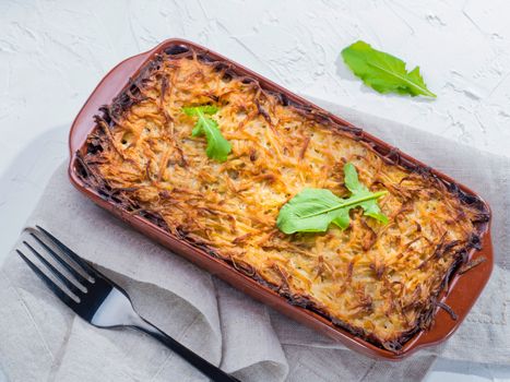 Close up view of appetizing potato casserole with fish, eggs and cream. Potato casserole in serving baking dish on white concrete background